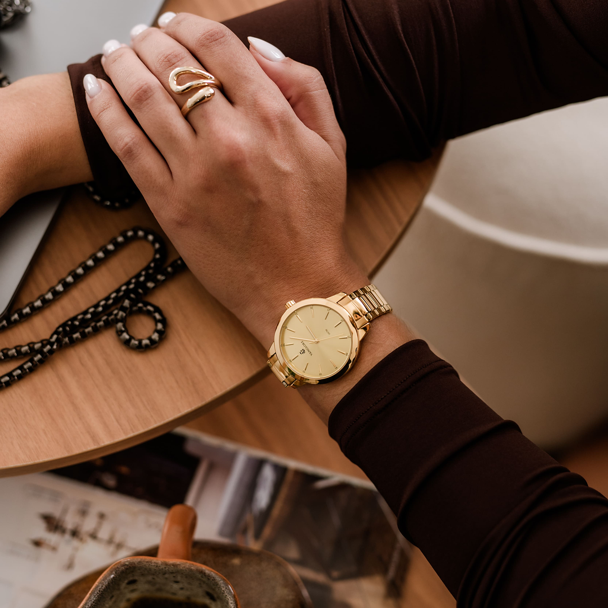 Relógio feminino Vanglore Essence dourado 36mm, no pulso, sobre a mesa