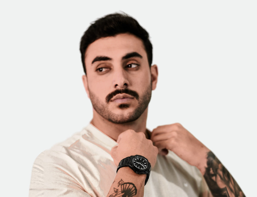 Homem de camiseta bege ajustando a gola, com o relógio Vanglore Legacy 4825a preto no pulso